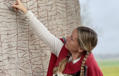 Vikingakvinna som pekar upp på Rökstenen.