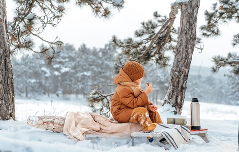 En liten pojke i bruna vinterkläder som sitter på en filt i ett vinterlandskap.