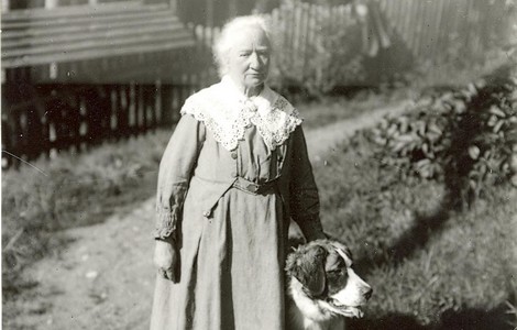 Ett svart vitt foto på författaren Ellen Key. På bilden ser man en äldre kvinna med klänning och vit spetskrage. Till vänster står en st. bernhardhund. 