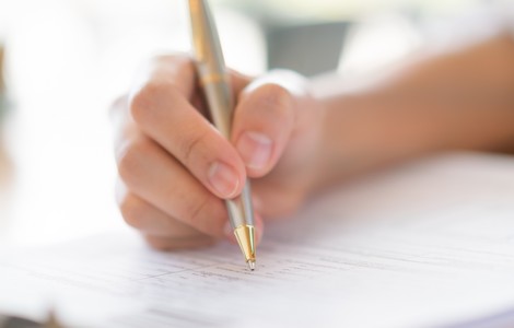 En person som skriver på ett dokument med en bläckpenna.
