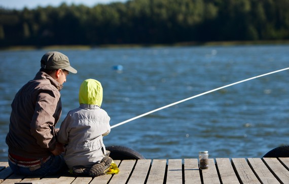 Far och son som sitter på en brygga och fiskar. 