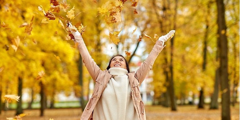 En glad tjej sträcker upp händerna i luften och kastar löv