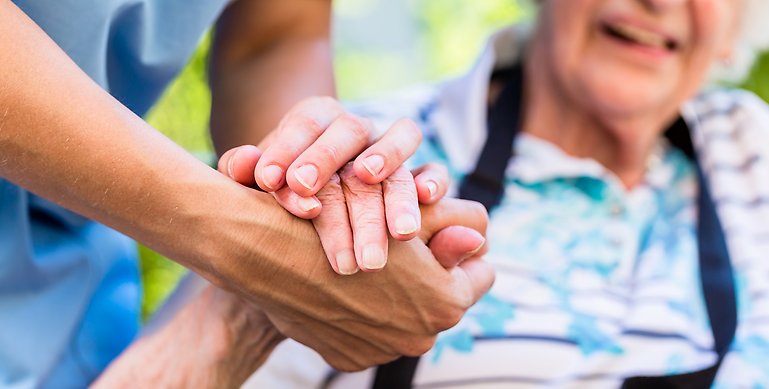 Händer som håller i varandra i en vårdsituation, en äldre och en yngre
