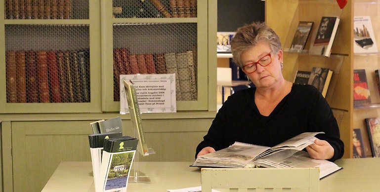 Anne-Sofie som sitter vid ett bord och läser en bok. 