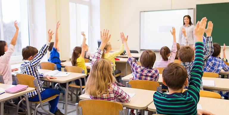 Barn i klassrum med uppsträckta händer