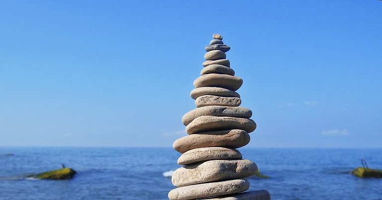 Platta stenar är uppbyggda som ett torn på en strand med vatten bakom