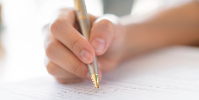 En person som skriver på ett dokument med en bläckpenna.