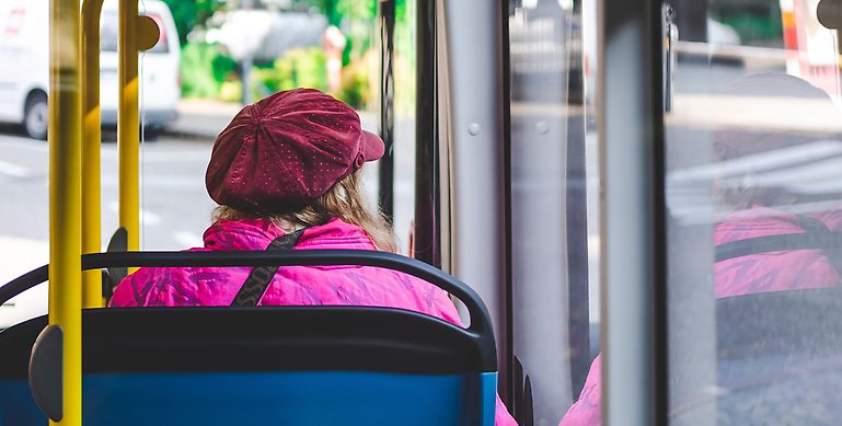En kvinna med rosa jacka och röd keps sitter i en buss.