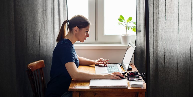En kvinna som sitter vid ett bord med sin dator.