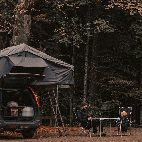 En man och en pojke som sitter med campingstolar vid ett tältplats.